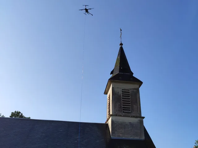 Église de village en pierre, drone en vol au-dessus du clocher, vue depuis le cimetière.