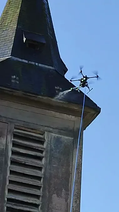 Le drone pulvérise le traitement sur la flèche en ardoise du clocher.