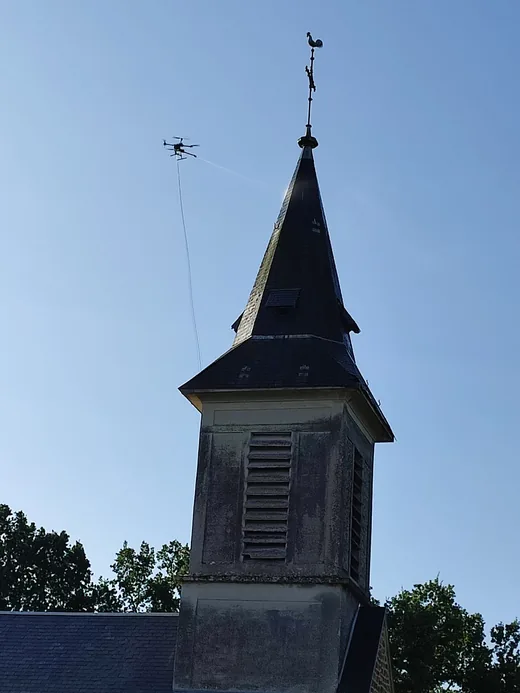 Vue rapprochée du drone en vol stationnaire près du clocher.