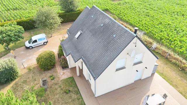 Maison contemporaine en ardoise vue du ciel, entourée de champs.