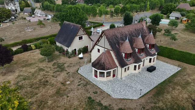 Vue aérienne oblique d'un manoir normand à colombages et tourelles, entouré de son parc.